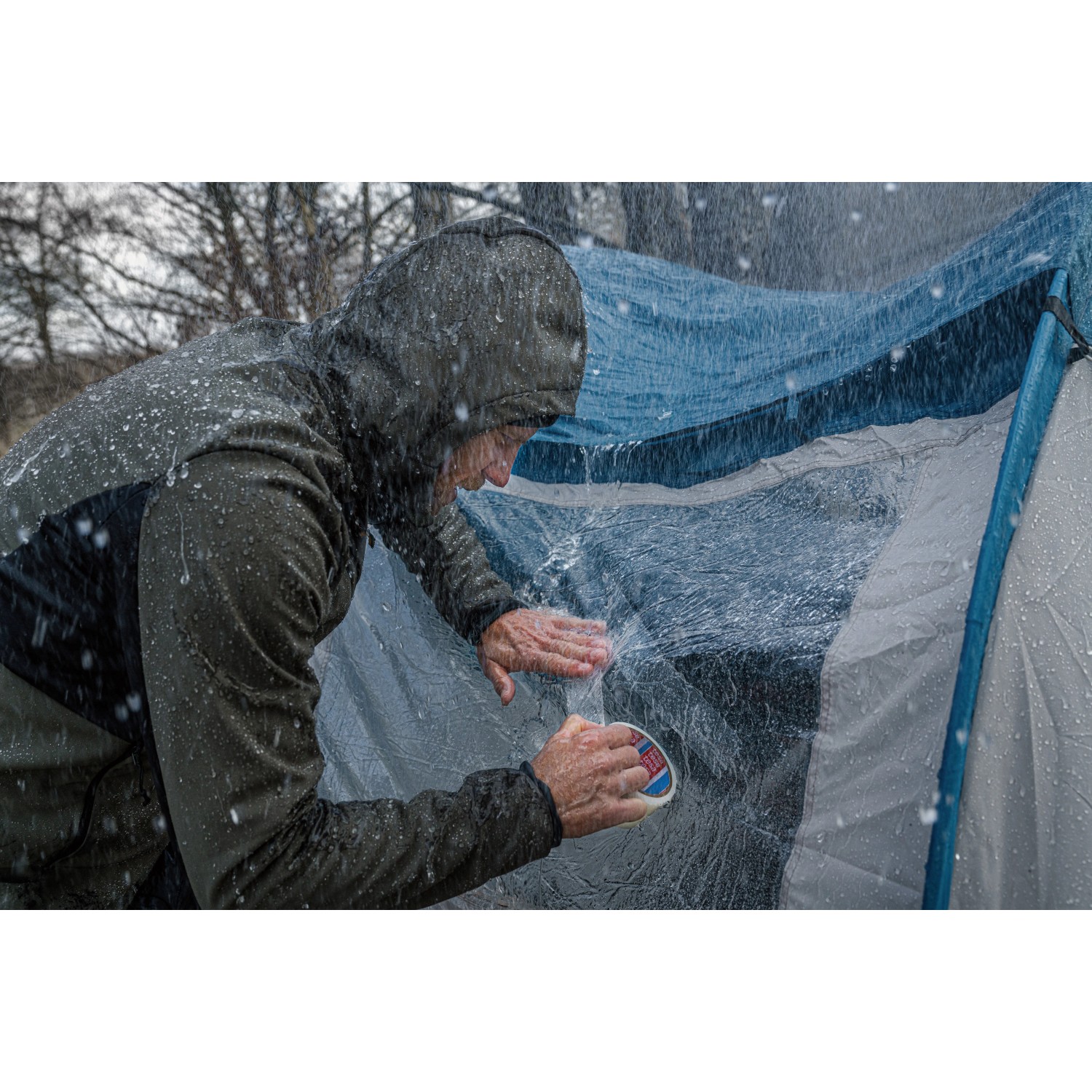 Mann repariert Zelt mit transparentem Tesa Ultra Power Clear Reparaturband bei Regen.