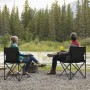Zwei Personen sitzen in schwarzen Sunula Campingstühlen am Flussufer.