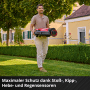 Mann trägt Einhell Freelexo 500 Mähroboter im Garten. Der Roboter ist rot und schwarz.