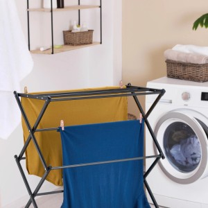 Schwarzer klappbarer Stahl-Wäscheständer mit gelber und blauer Wäsche in einer Waschküche. Platzsparendes Design.