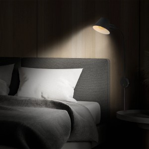 Schwenkbare, schwarze Briloner Bettleuchte neben einem Bett mit weißem Kissen.