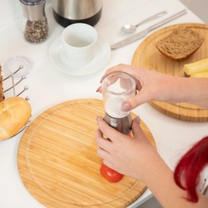 Hände nutzen Relaxdays Glas-Edelstahl-Mühle auf Holzbrett. Pfeffer- & Salzmühlen 2er Set für Küche.