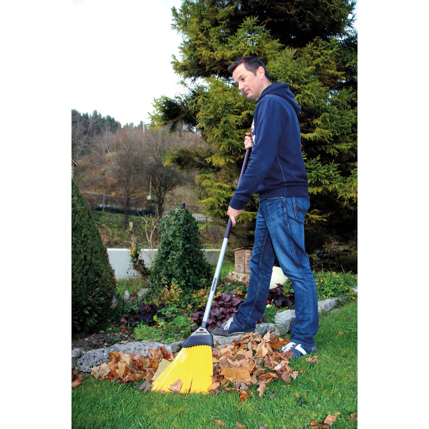Mann kehrt Laub mit gelbem Sonneck Universalbesen mit Stiel im Garten.