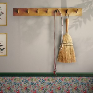 Detailaufnahme der Joules Vliestapete Uni in Grau-Beige mit floraler Bordüre und Garderobe.