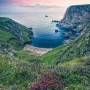 Komar Fototapete Vlies The Blue Bay: Küstenlandschaft mit blauem Meer und grünen Klippen bei Sonnenaufgang.