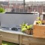 Lechuza Balconera Stone 50 Blumenkasten, steingrau, mit Pflanzen und Zubehör auf einem Gartentisch.