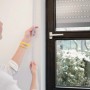 Frau misst Rollladengurt Maxi 23mm Grau am Fenster aus.