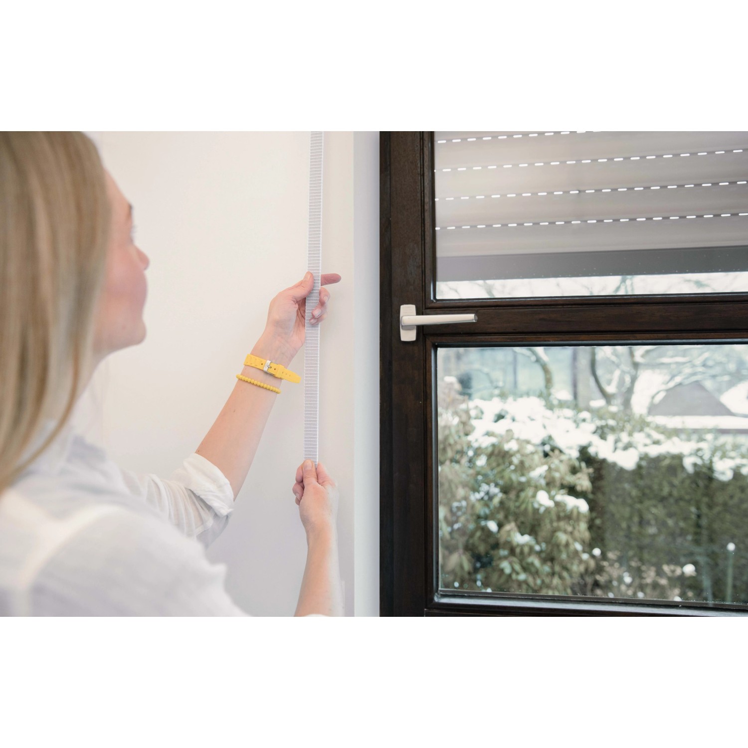 Frau misst Rollladengurt Maxi 23mm Grau am Fenster aus.