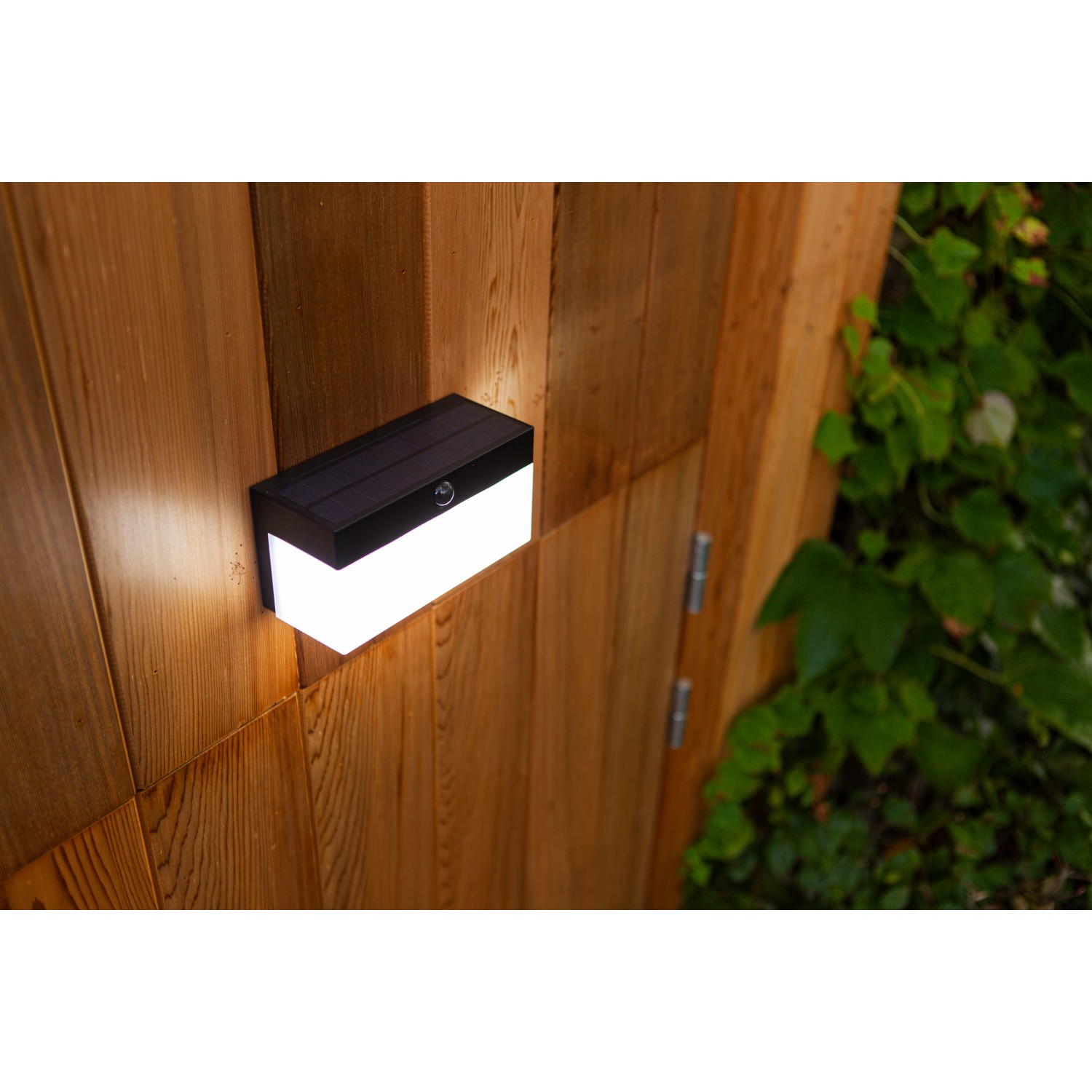 Schwarze Lutec LED Solar-Wandleuchte Fran an Holzwand. Moderne, eckige Außenleuchte mit Bewegungsmelder.