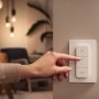 Weißer Philips Hue Dimmschalter V2 an Wand, Finger drückt Taste. Smart Home Beleuchtung steuern.