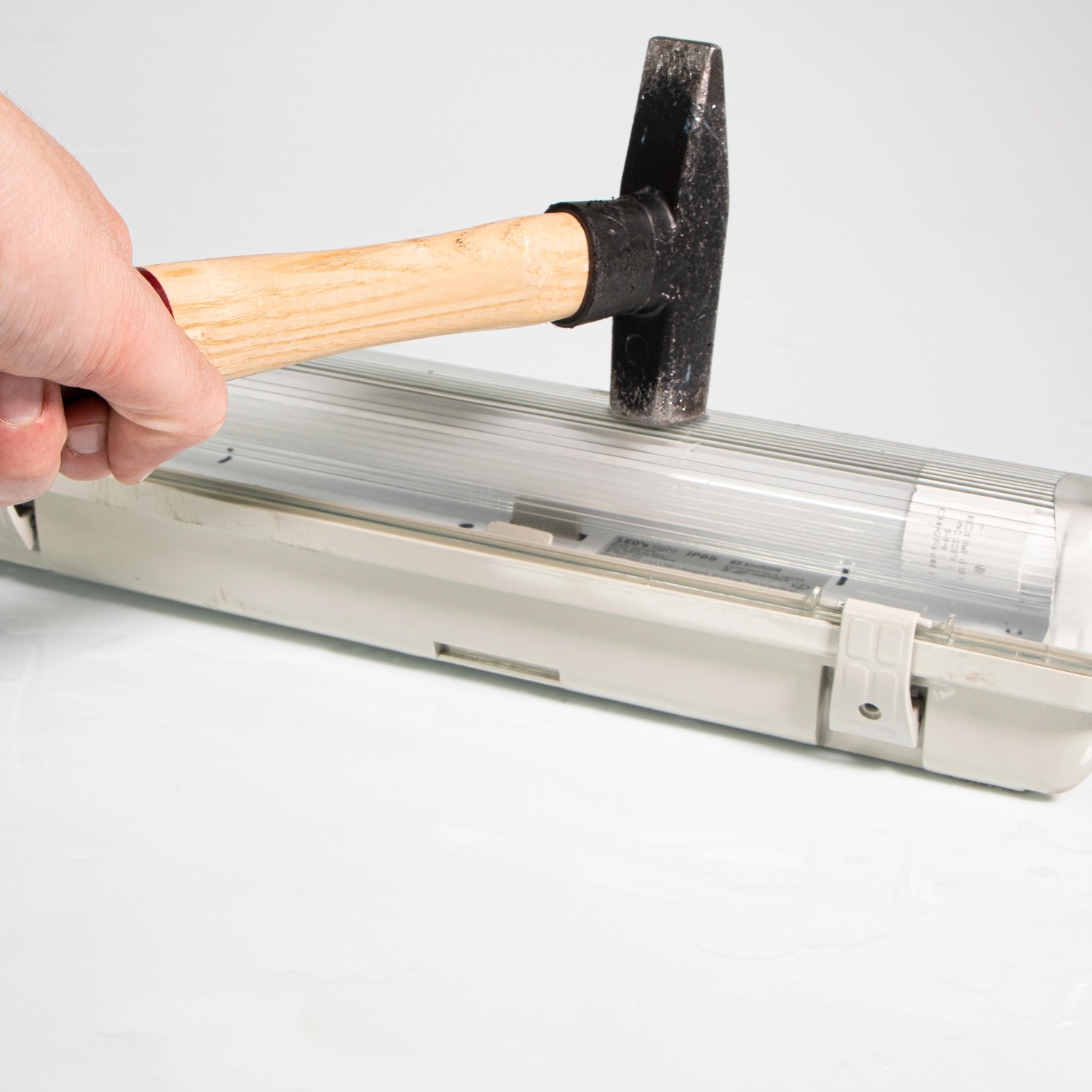 Hammer schlägt auf graue LED-Feuchtraumleuchte 120cm. Schlagfestigkeitstest.