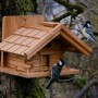 Holz-Vogelhaus „St. Moritz“ im Berghütten-Design mit zwei Meisen am Baum.
