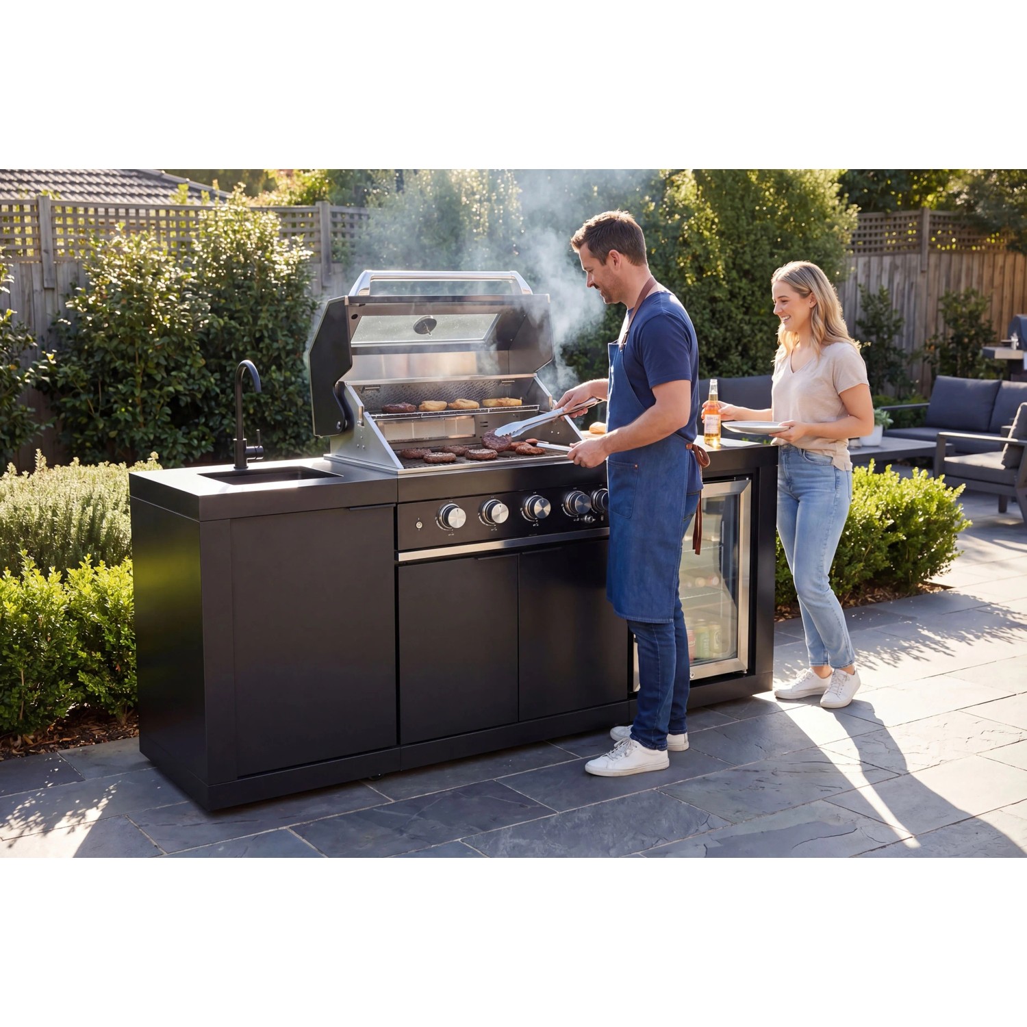 Buschbeck Outdoorküche Liverpool Schwarz mit Grill, Spüle und Kühlschrank im Garten.