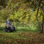 Alpina Rasentraktor AT3 98 A in Aktion: Frau fährt auf Rasenfläche mit Bäumen.