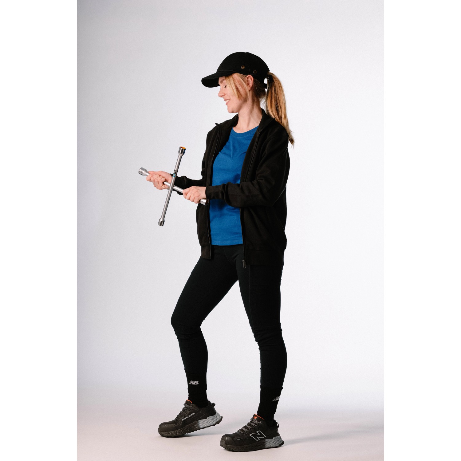 Frau mit New Balance Sicherheitsschuhen Cremorne S3L in Schwarz-Grau und Schraubenschlüssel.