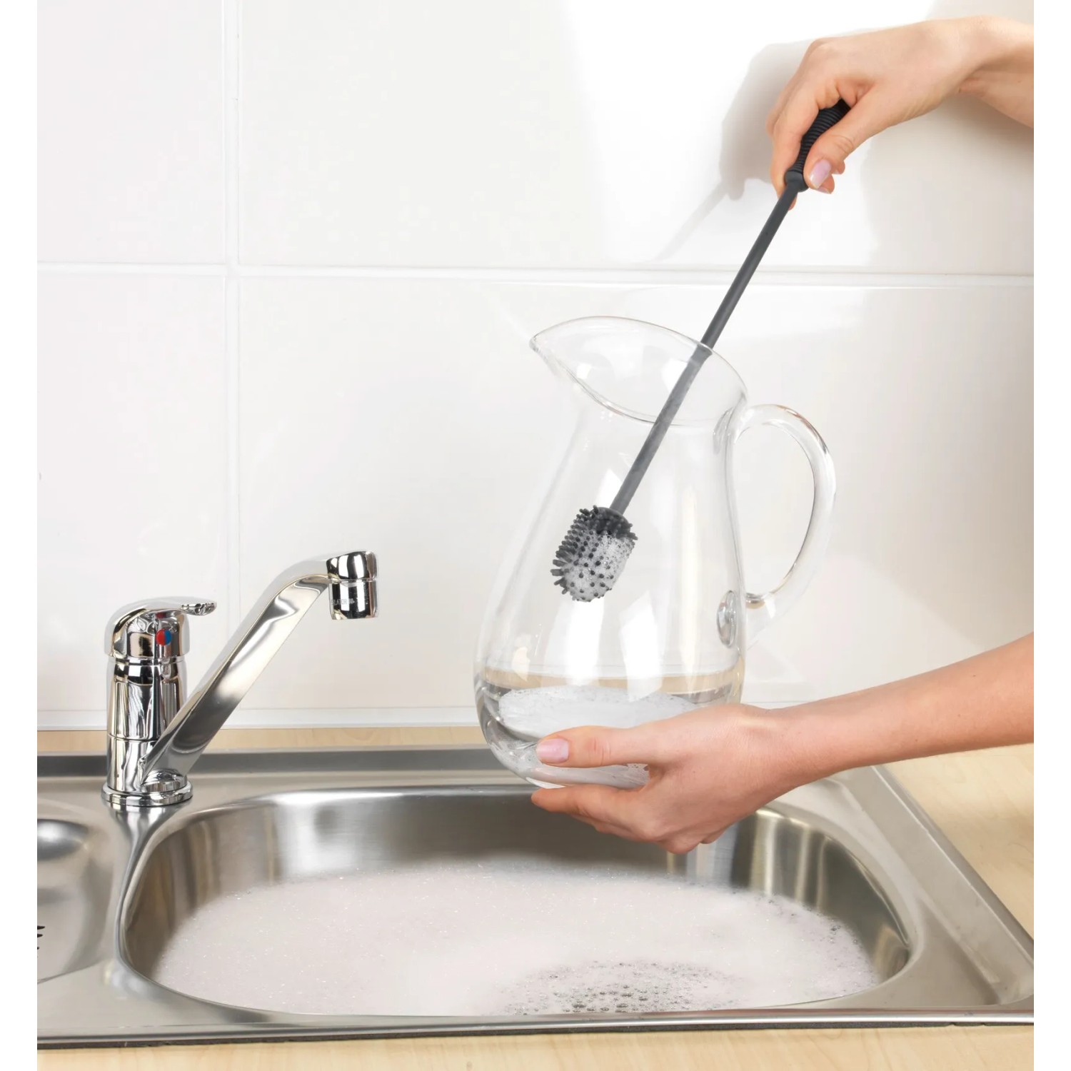 Anthrazitfarbene Wenko Silikon Flaschenbürste (38 cm) reinigt eine Glaskaraffe in der Spüle.