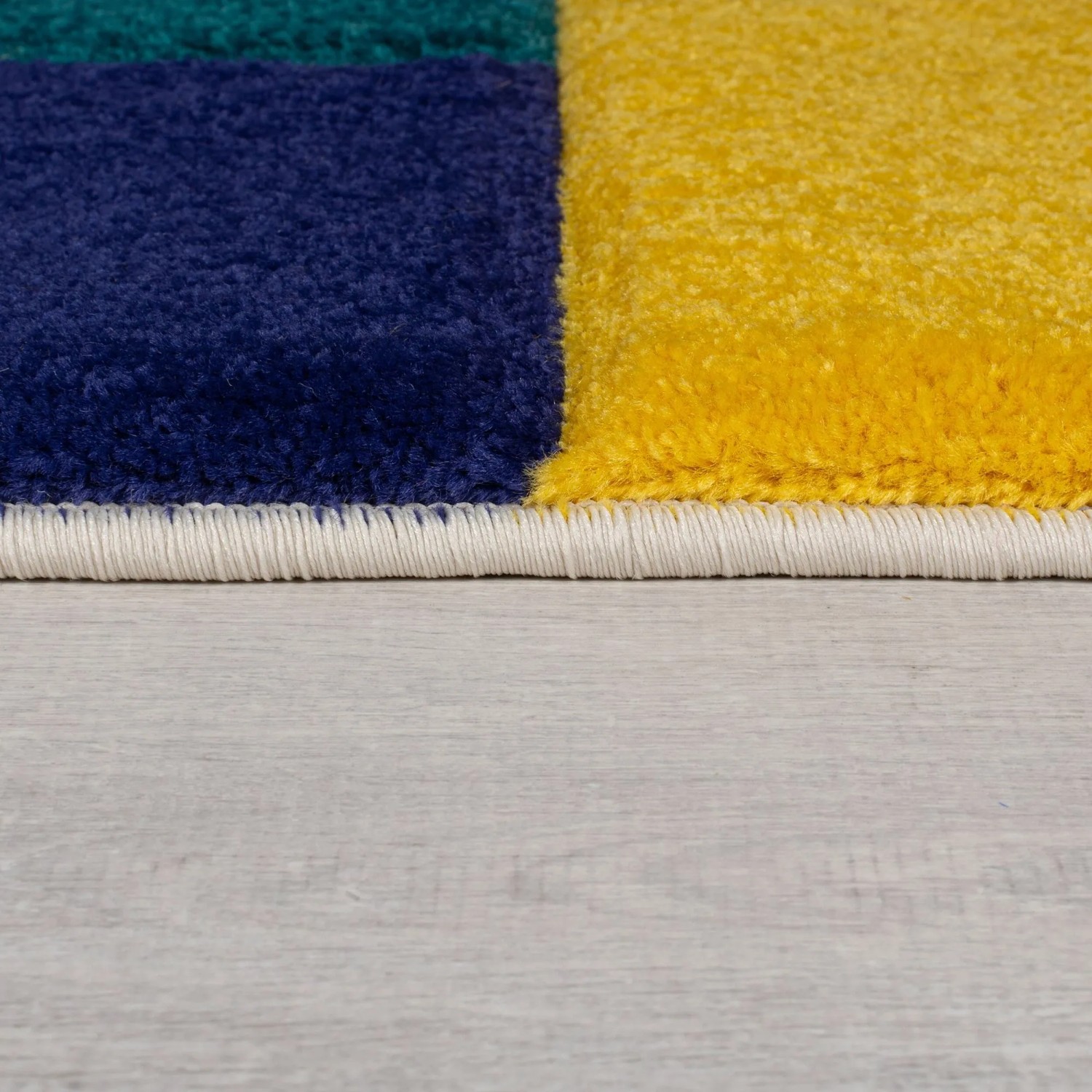 Flair Rugs Kinderteppich Mambo: Nahaufnahme bunter, geometrischer Blöcke in Blau, Gelb, Grün mit weißem Rand auf Holz.