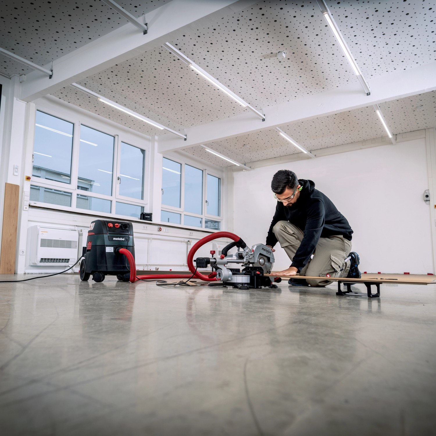 Mann arbeitet mit Metabo Kappsäge KGS 216 M Set und Staubsauger in Werkstatt.