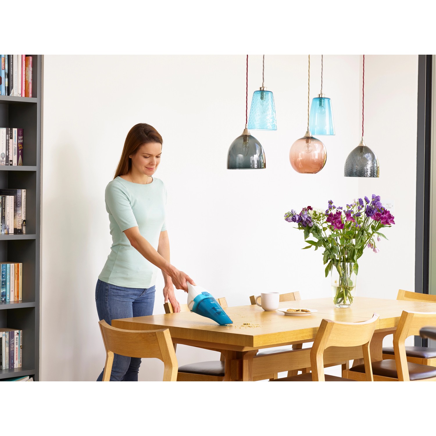 Frau saugt Krümel mit Black+Decker Akku-Nass-/Trockensauger vom Holztisch.