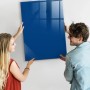 Blaue Glasmagnettafel 70x100 cm wird von zwei Personen an der Wand befestigt.