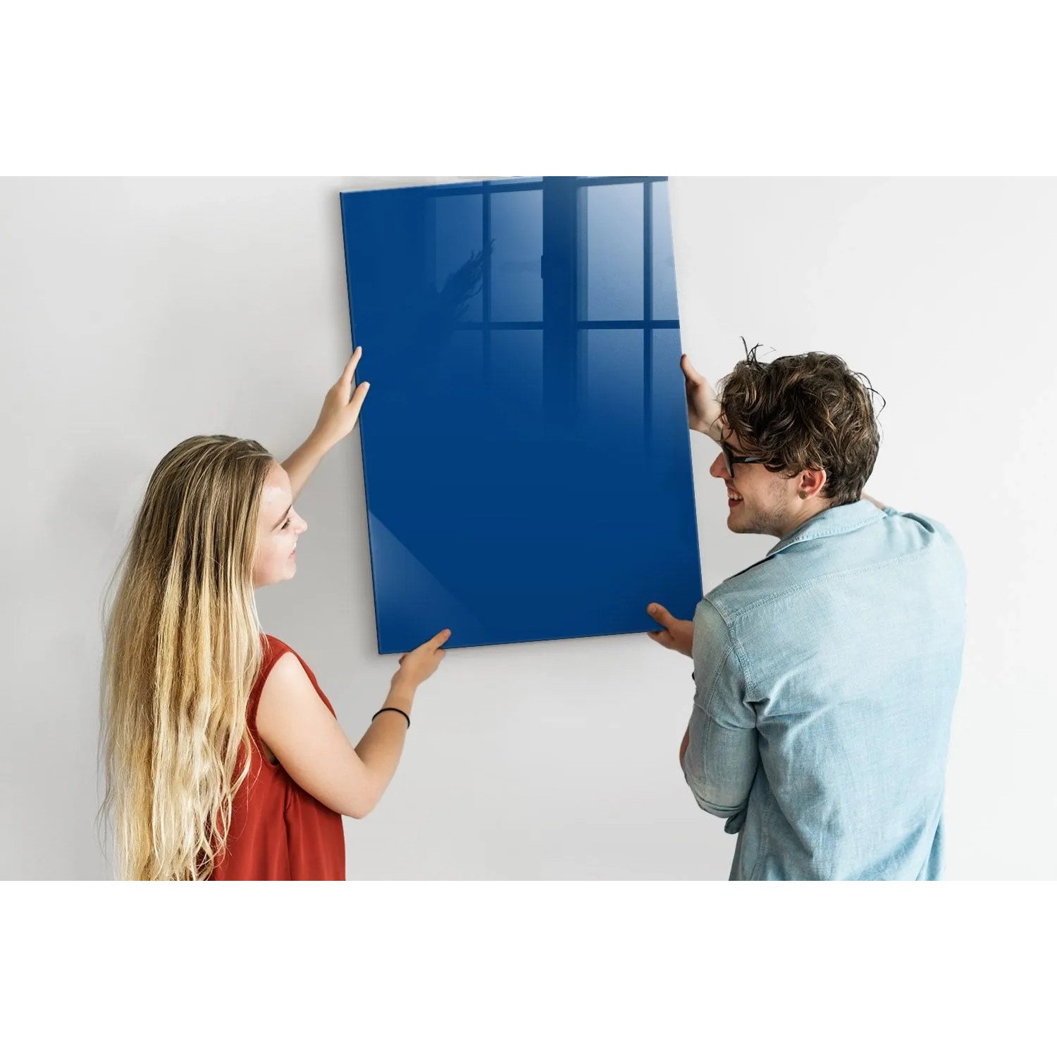 Blaue Glasmagnettafel 70x100 cm wird von zwei Personen an der Wand befestigt.
