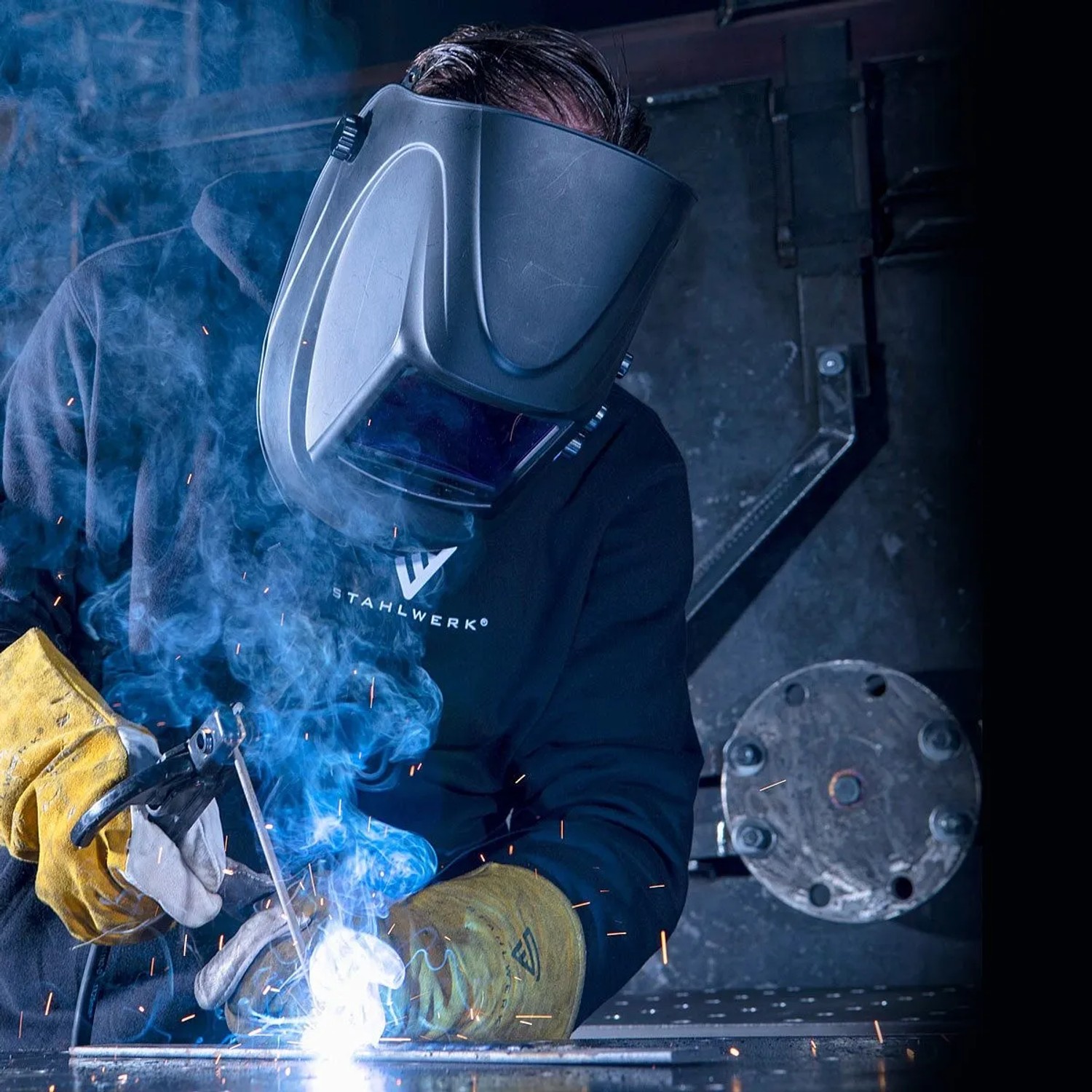Schweißer mit STAHLWERK Schweißhelm und Handschuhen beim Schweißen. Funken und Rauch. ARC 200 Puls Pro Schweißgerät im Einsatz.