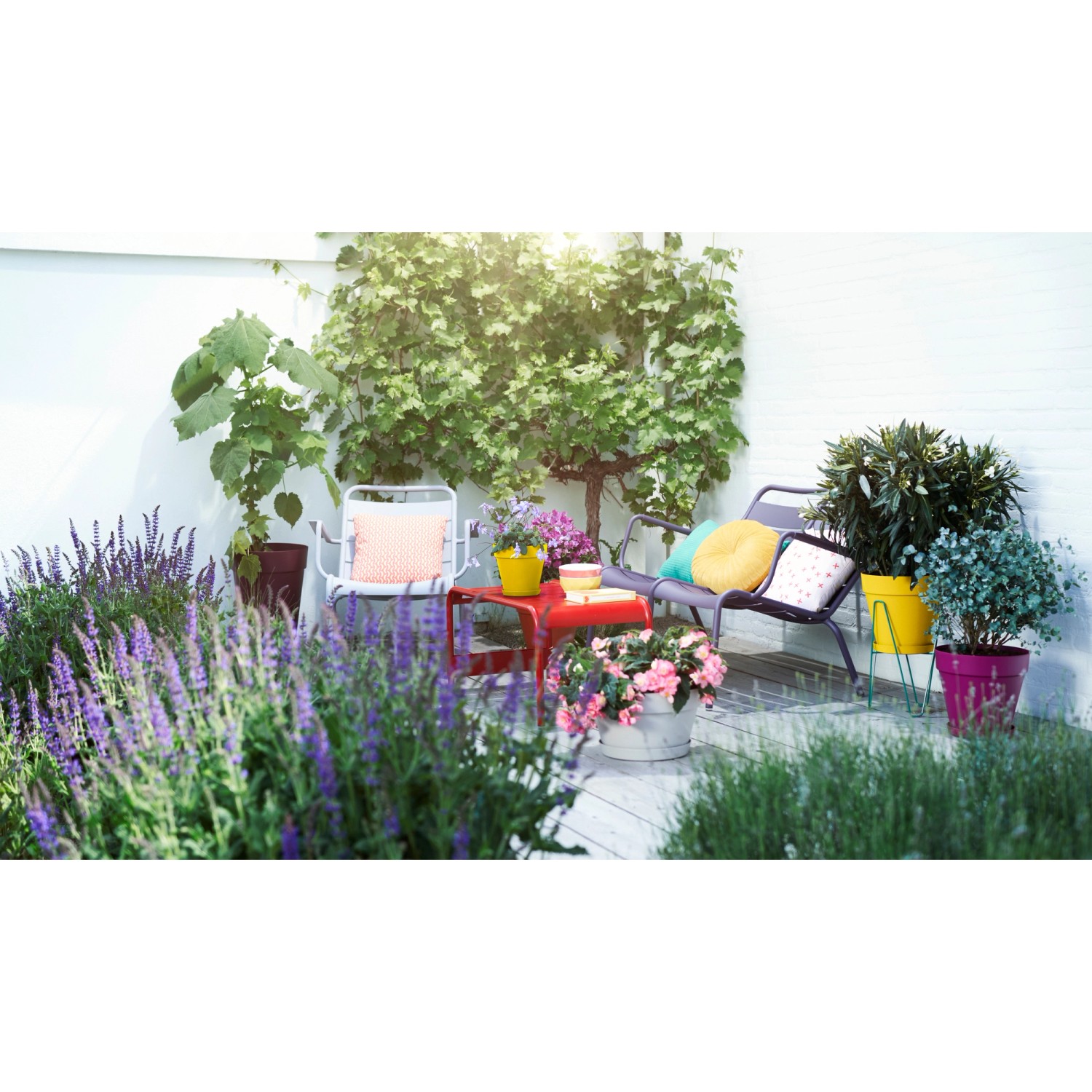 Szene mit Elho Loft Urban Blumentöpfen in Ocker und anderen Farben auf einer Terrasse mit Pflanzen.