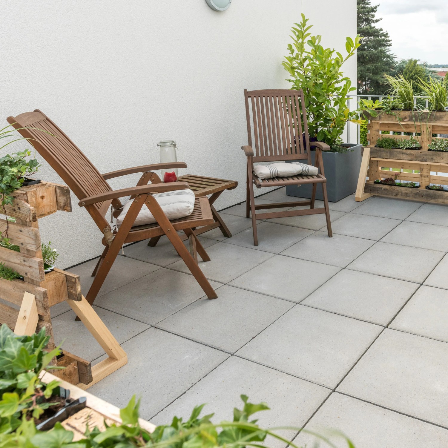 Verlegte, graue Gehwegplatten 30x30 cm mit Fase auf einer Terrasse mit Gartenmöbeln.