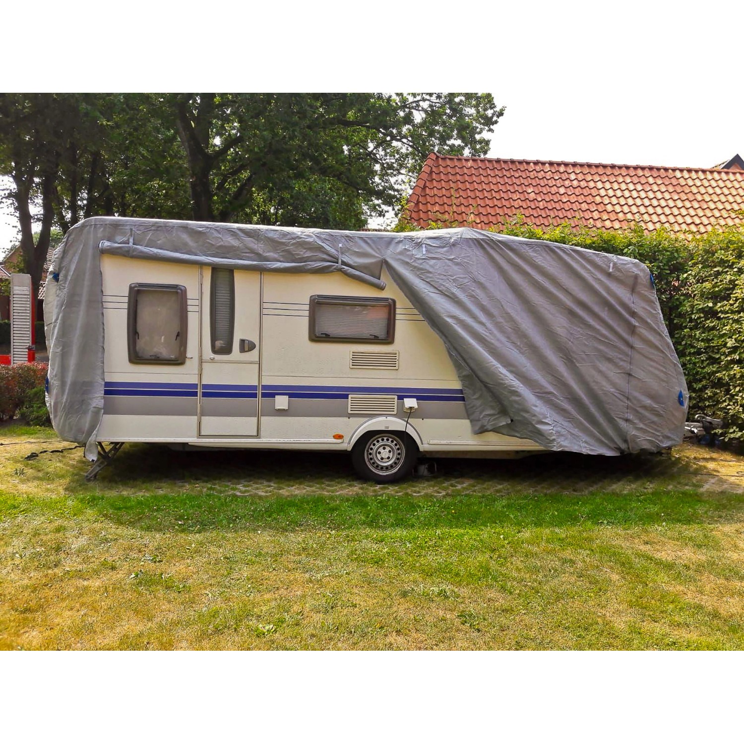 Graue Garden Pleasure Wohnwagen Abdeckhaube Größe L schützt einen Wohnwagen auf einer Wiese.