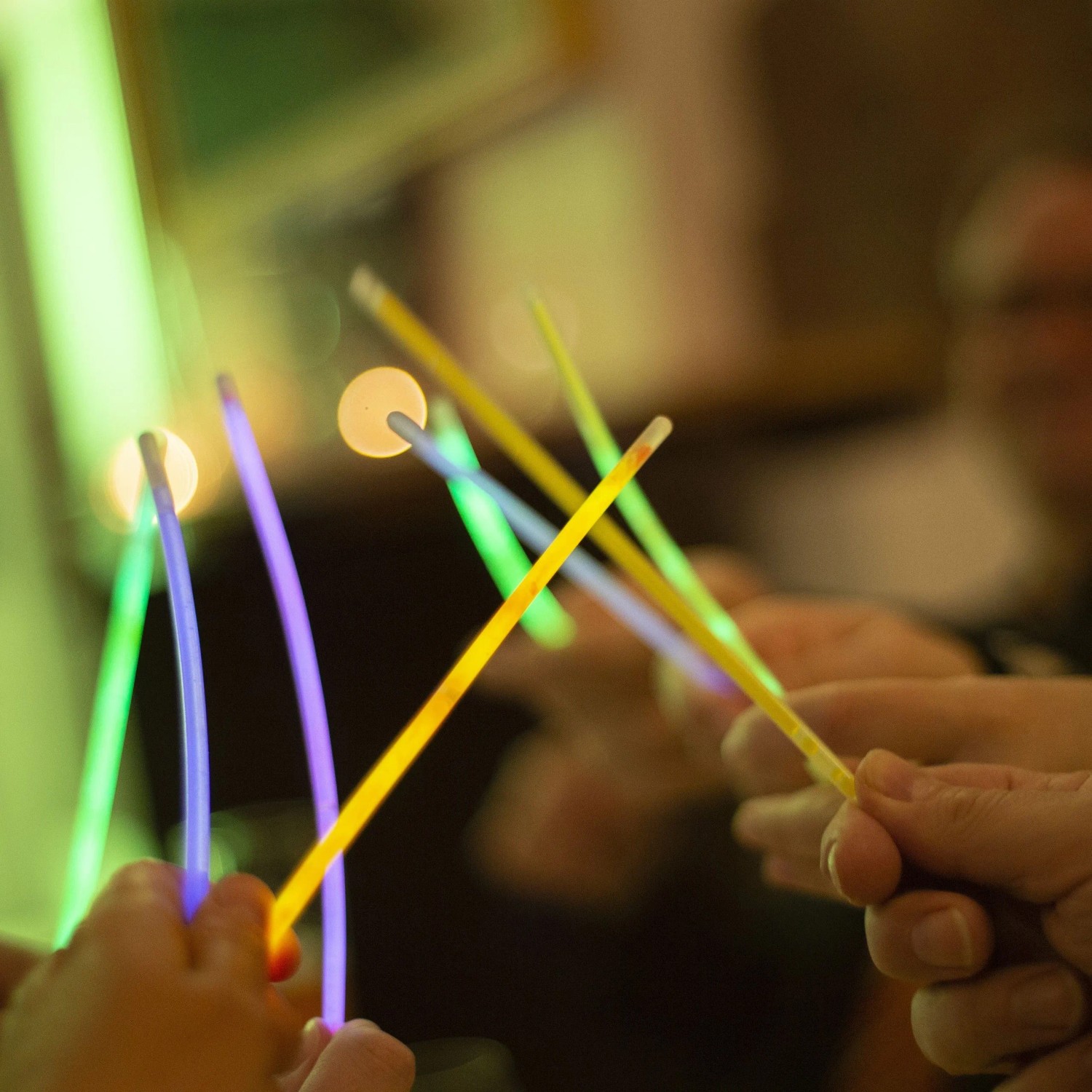 Bunte Knicklichter in Händen auf einer Party. Leuchtstäbe in Grün, Lila, Gelb sorgen für festliche Stimmung.