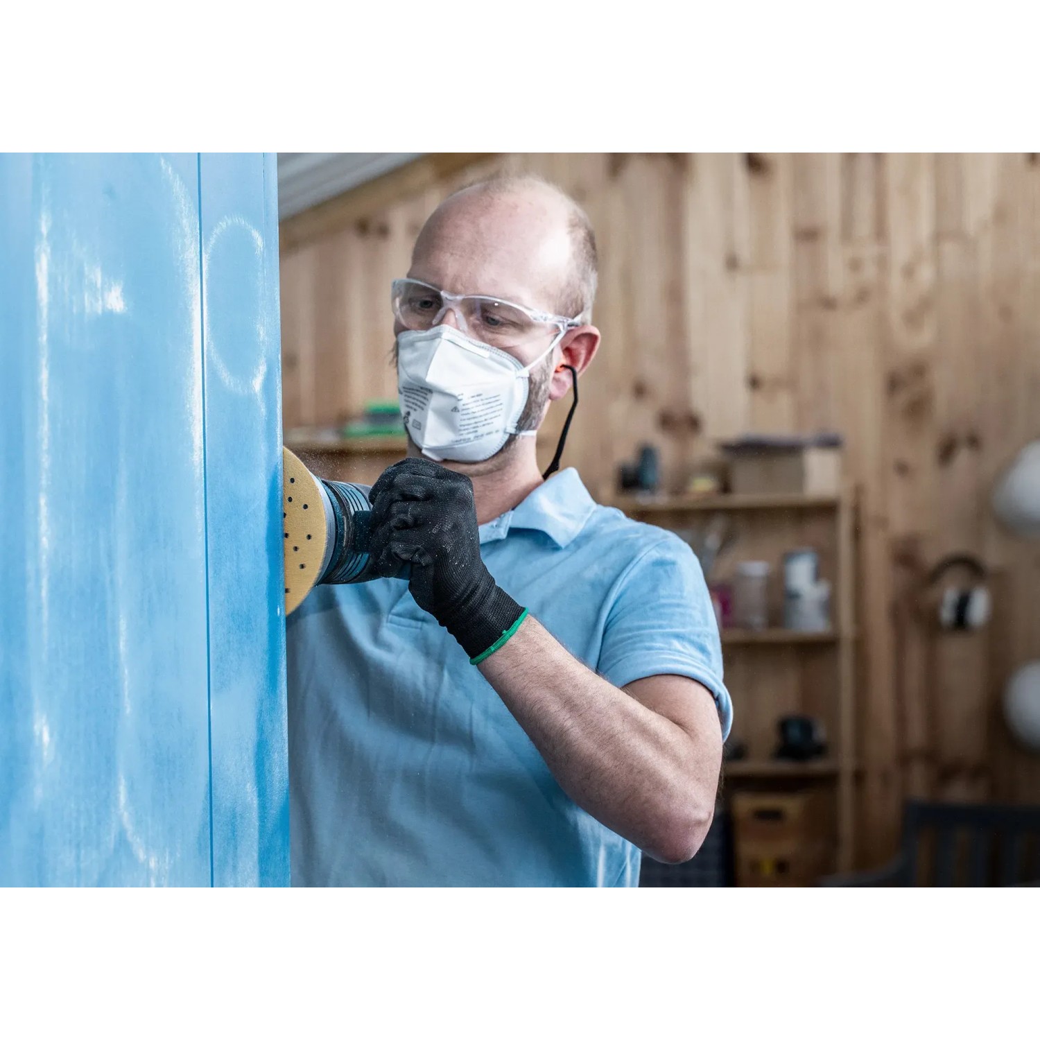 Mann schleift blaue Holzoberfläche mit Bosch Expert Schleifblatt C470 und Exzenterschleifer.