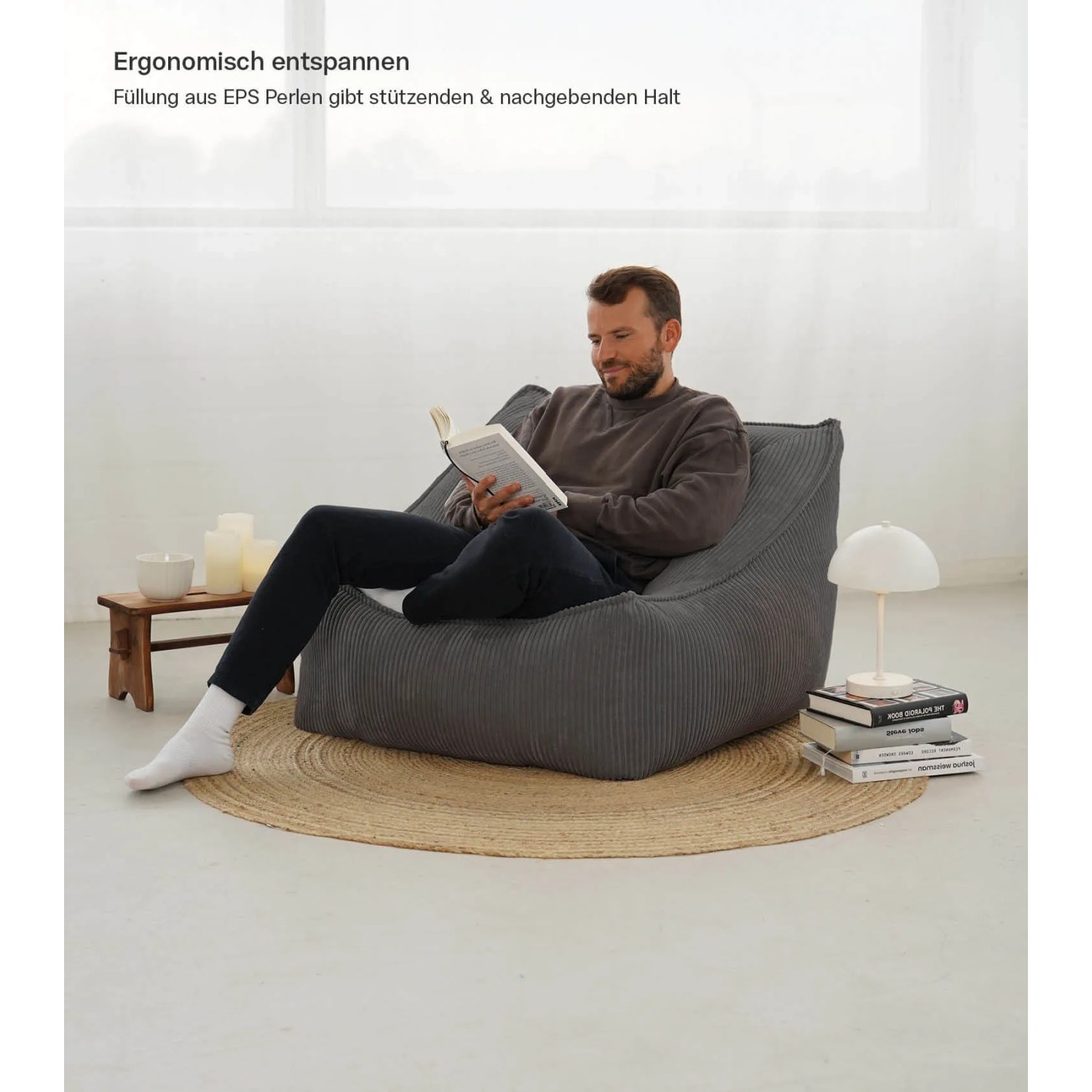 Mann liest entspannt im anthrazitfarbenen mokebo Cord Sitzsack Sessel mit Hocker.
