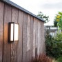 Moderne Lutec LED-Außenwandleuchte Qubo an einer Holzwand im Garten.