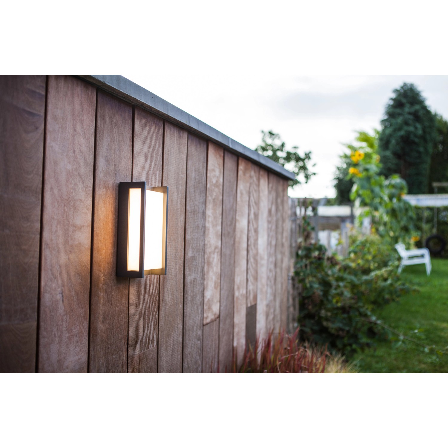 Moderne Lutec LED-Außenwandleuchte Qubo an einer Holzwand im Garten.