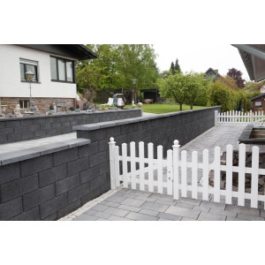 Anthrazitfarbene EHL Planomur Mauer aus Normalsteinen mit weißem Zaun im Garten.