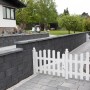 Anthrazitfarbene EHL Planomur Mauer aus Normalsteinen mit weißem Zaun im Garten.