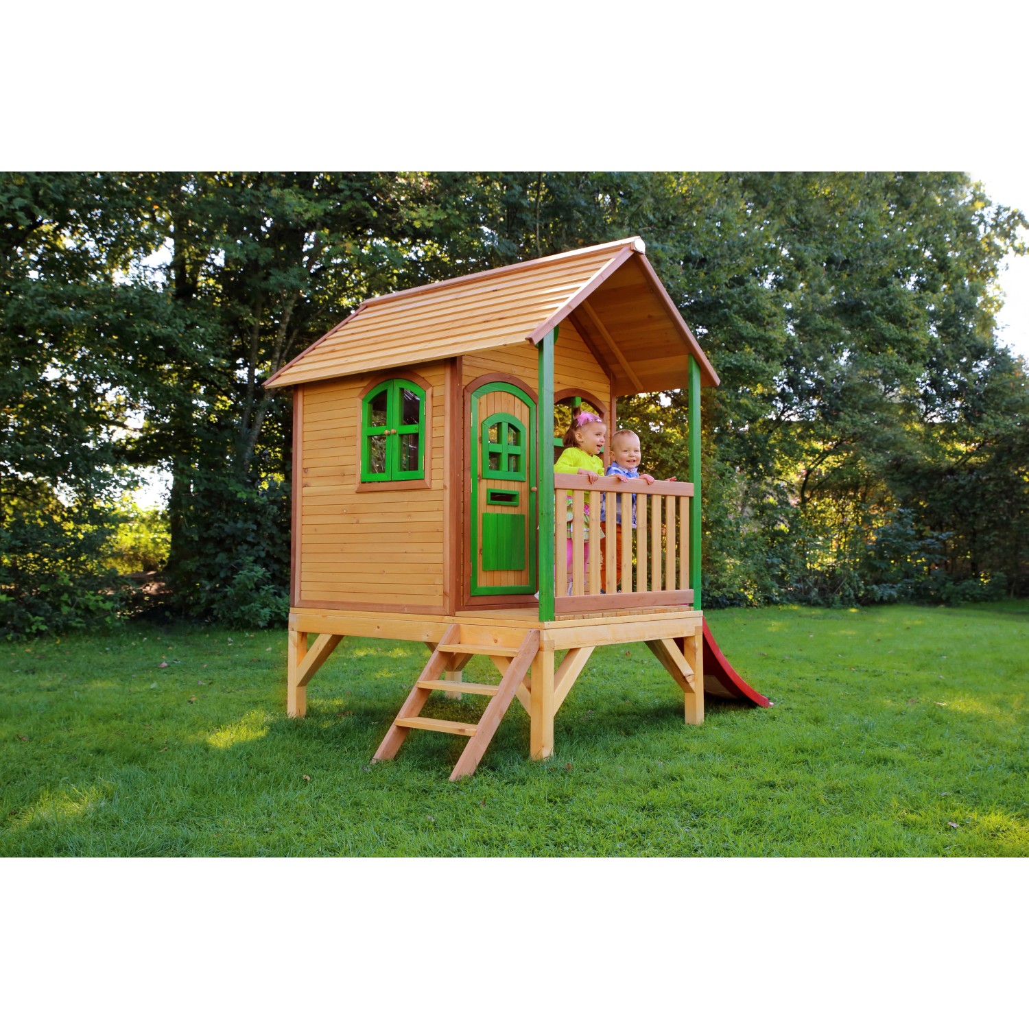 Axi Tom Spielhaus aus Holz mit roter Rutsche, braun und grün, mit zwei Kindern auf der Veranda.