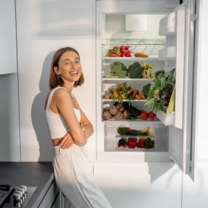Offener Kühlschrank mit Gemüse und Obst, daneben eine Frau. Kühlschrank Organizer zur Aufbewahrung.