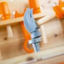 Kinderhammer schlägt grauen Steckstift in OBI Kinderwerkbank aus Holz. Orange Spielzeugwerkzeuge im Hintergrund.