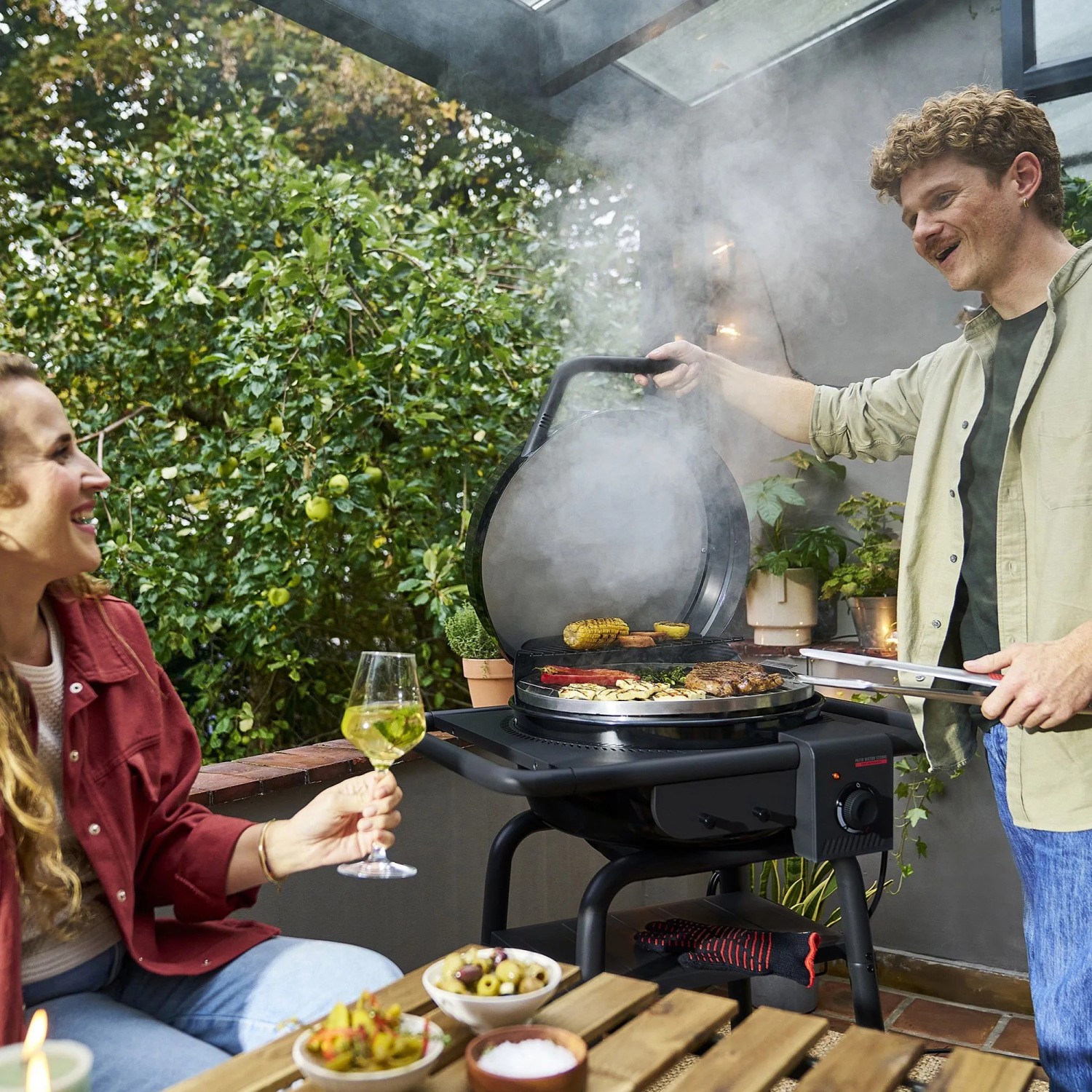 Schwarzer Char-Broil Elektrogrill Patio Bistro E2Coal beim Grillen mit Personen.