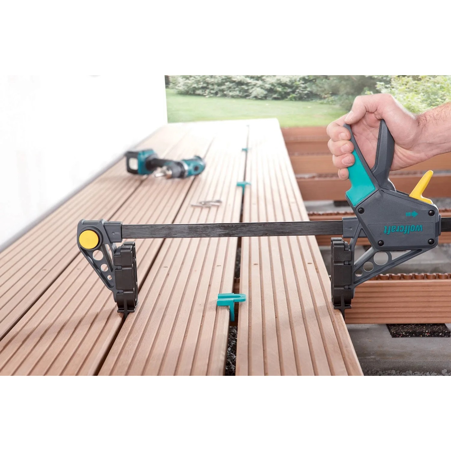 Wolfcraft Terrassenbau Set im Einsatz: Montagezwinge fixiert Terrassendielen, Abstandshalter sichtbar.