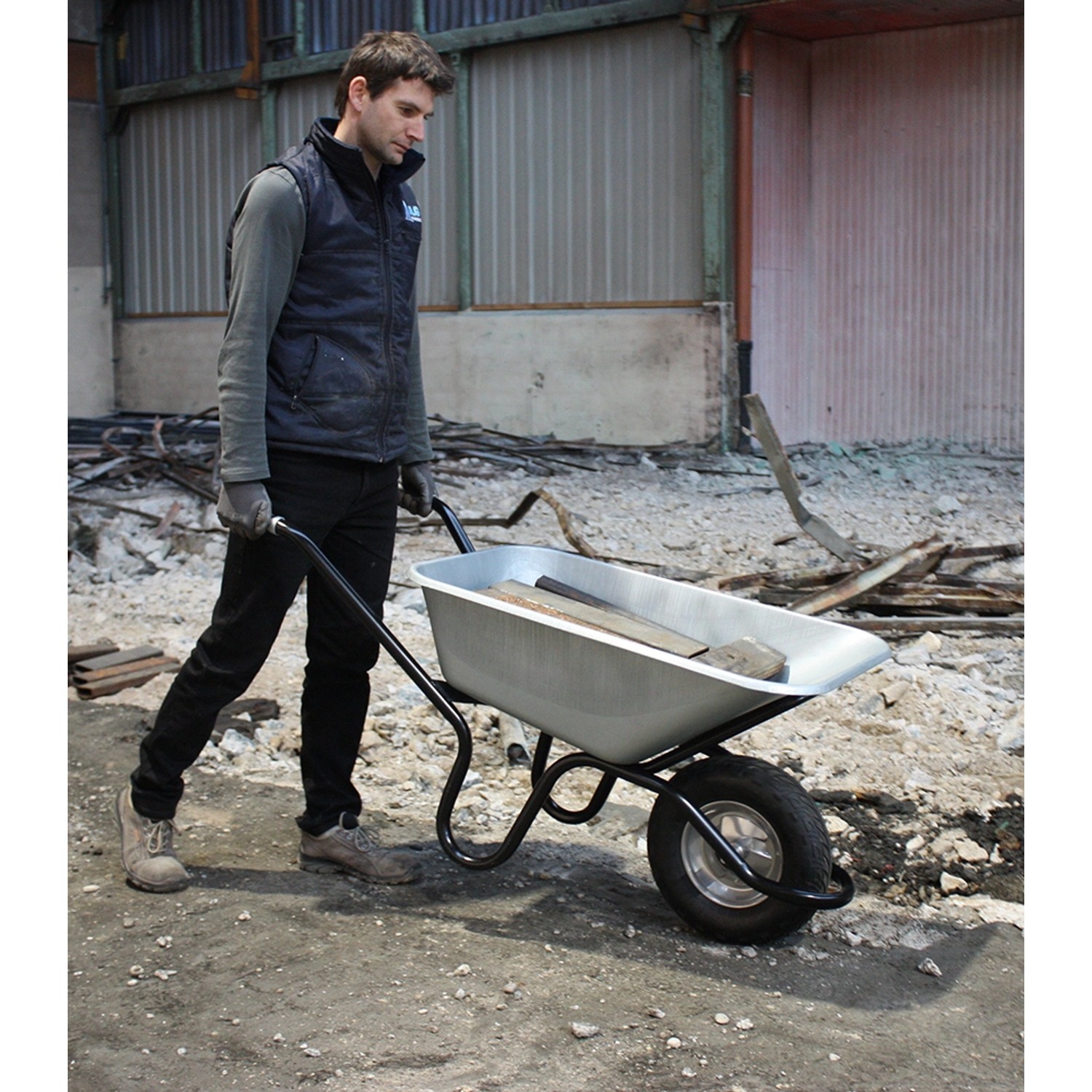 Mann schiebt Haemmerlin Schubkarre Bau Plus 120 l mit Luftrad und verzinkter Mulde.