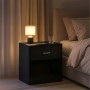 Schwarzer Relaxdays Nachttisch aus MDF mit Schublade und offenem Fach. Darauf Lampe, Handy, Glas neben einem Bett.
