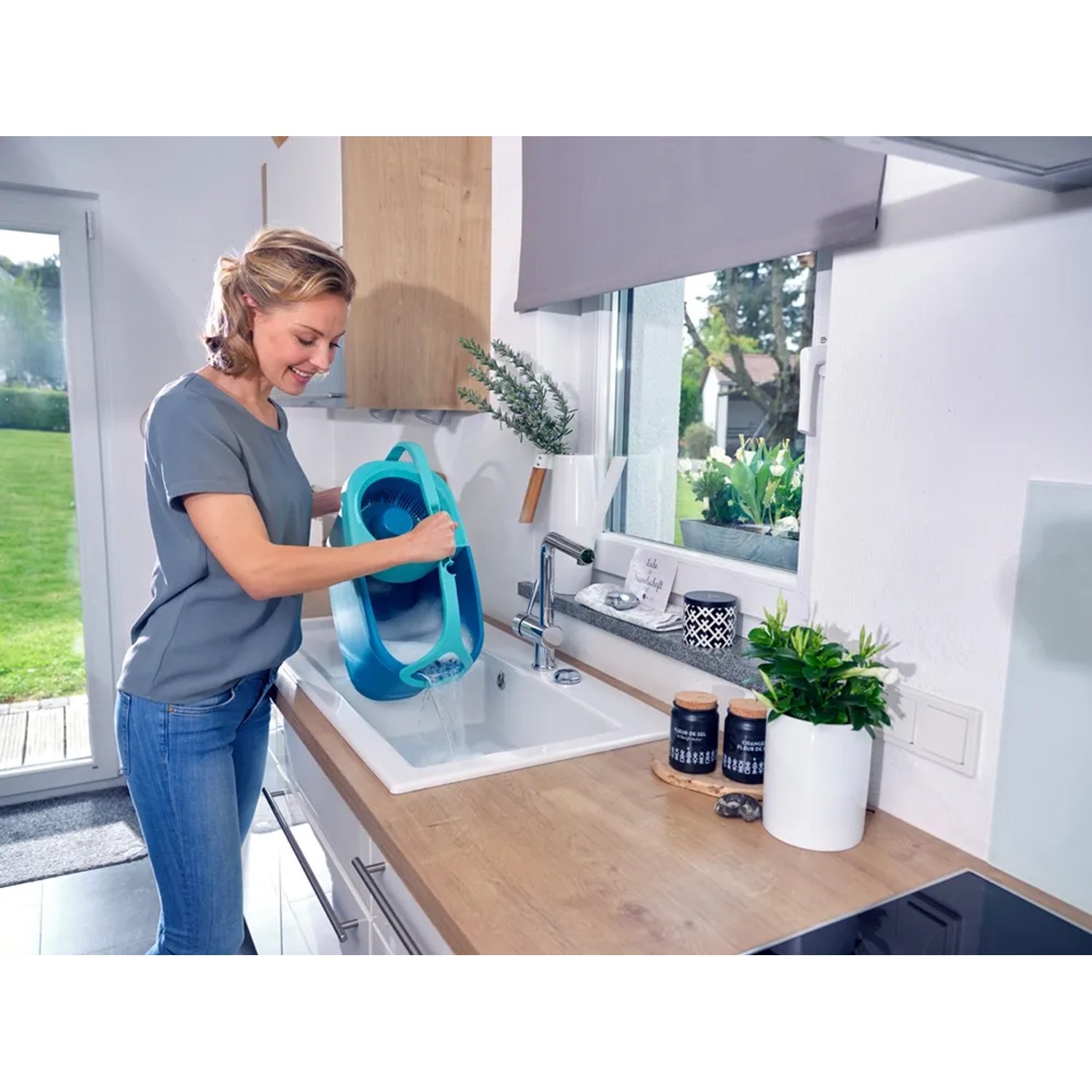 Frau leert blauen Leifheit Clean Twist Disc Mop Eimer in ein Waschbecken. Reinigungsgerät mit Schleuder.