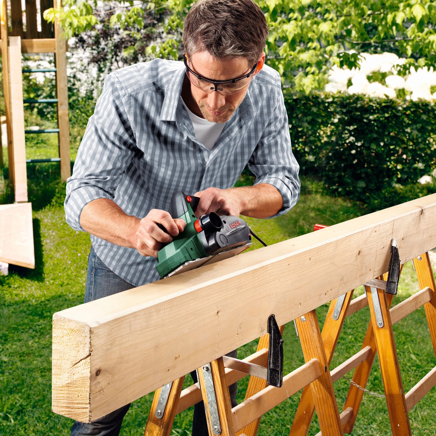 Mann hobelt Holz mit dem Bosch Elektrohobel PHO 2000 im Garten.