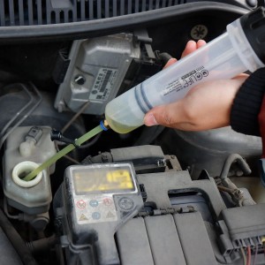 Transparente Ölabsaugspritze im Motorraum, eine Hand pumpt gelbe Flüssigkeit um. Ideal für Ölwechsel und Wartung.