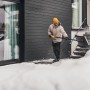 Mann räumt mit Fiskars Schneeräumer Solid Schnee vor Haus. Schneeschieber mit D-Griff.