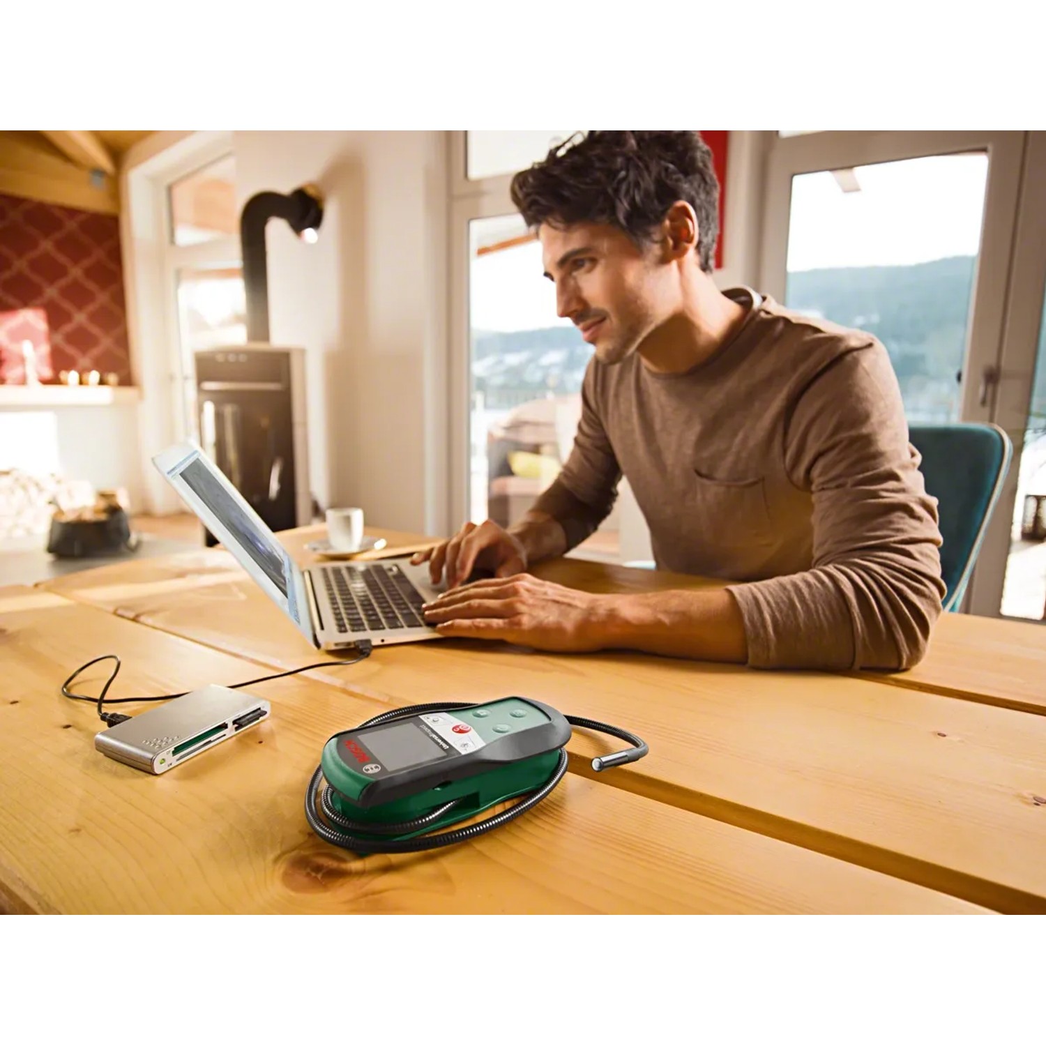 Bosch UniversalInspect Inspektionskamera mit Zubehör und Mann am Laptop auf Holztisch.