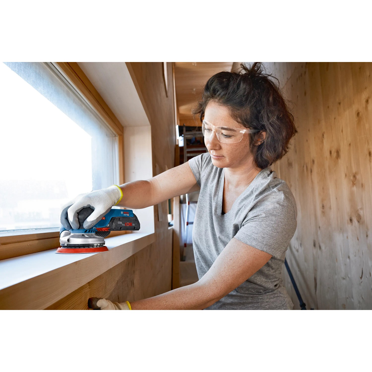 Frau schleift Fensterrahmen mit Bosch Professional Akku-Exzenterschleifer GEX 18V-125.