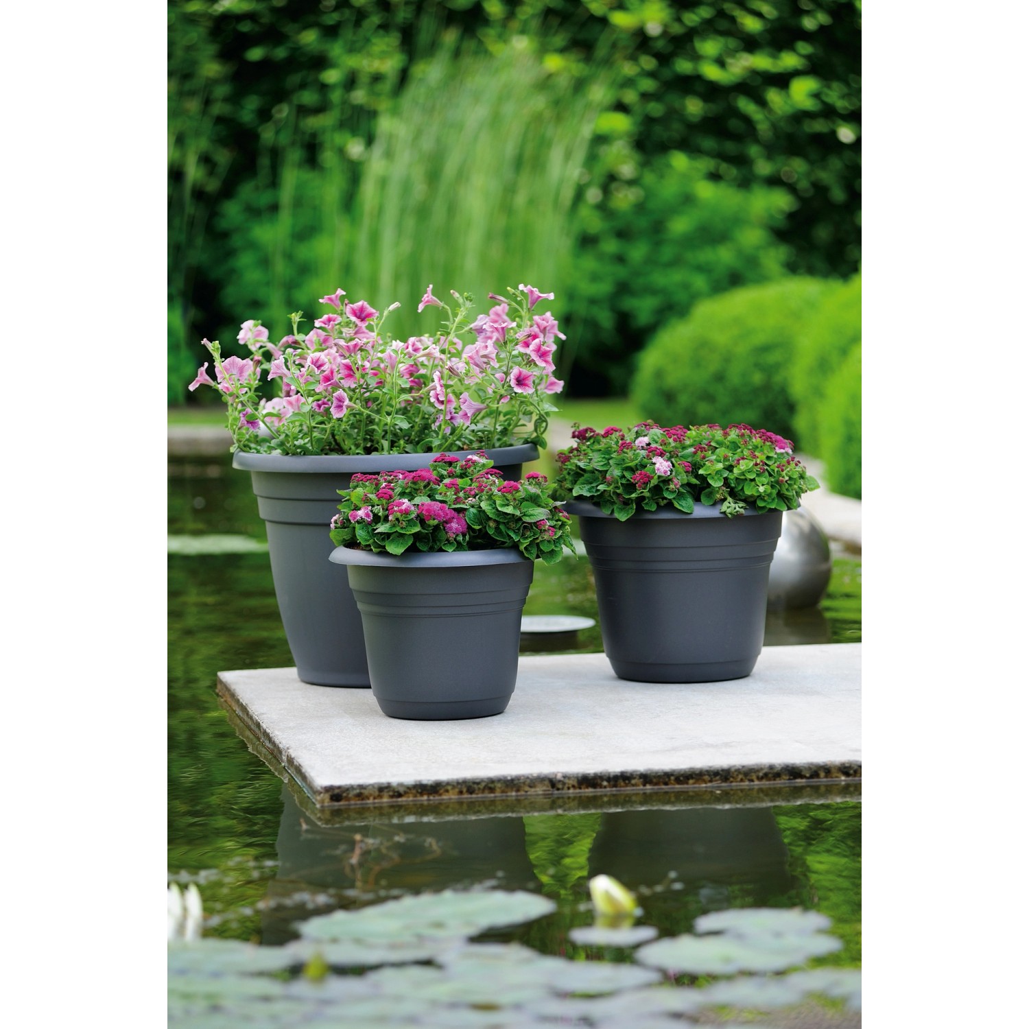 Anthrazitfarbene Florus Pflanztöpfe Fiore Alessia (Ø 55 cm) mit bunten Blumen auf einer Terrasse.